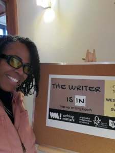 a picture of the poet stephanie roberts smiling next to a promotional The Writer is in sign.